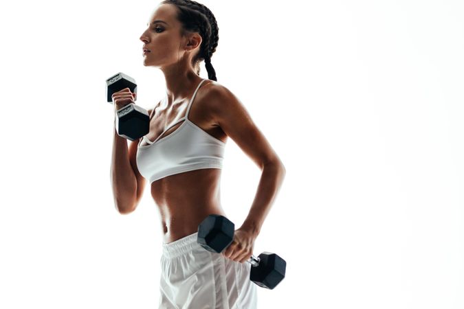 Fit woman lifting dumbbell weights against light background