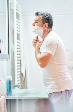 Man shaving beard with razor in bathroom