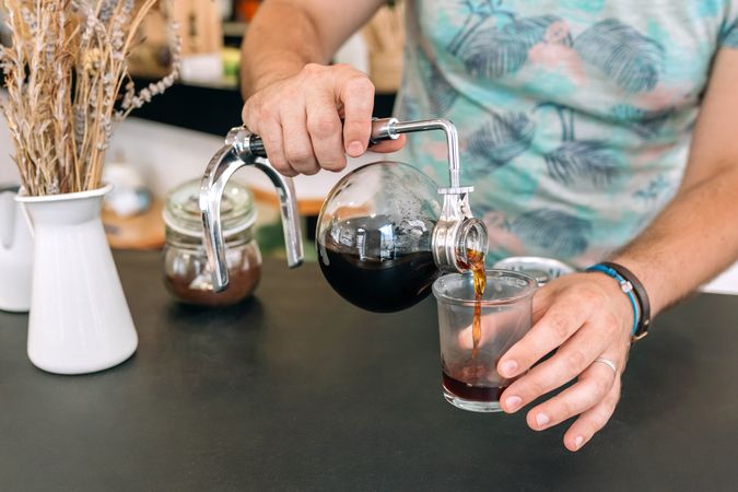 Unrecognizable barista pouring specialty coffee from Japanese siphon coffee maker into a glass