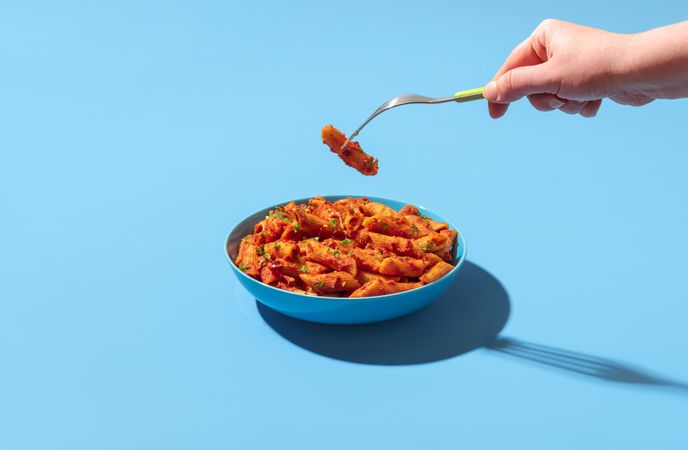 Eating pasta penne alla arrabbiata from a bowl, minimalist on a blue background