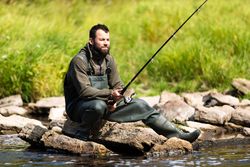 Fisherman Sitting on Rocks by River