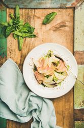 Top view of ham and pear in bowl, on green trimmed wooden board with linen napkin