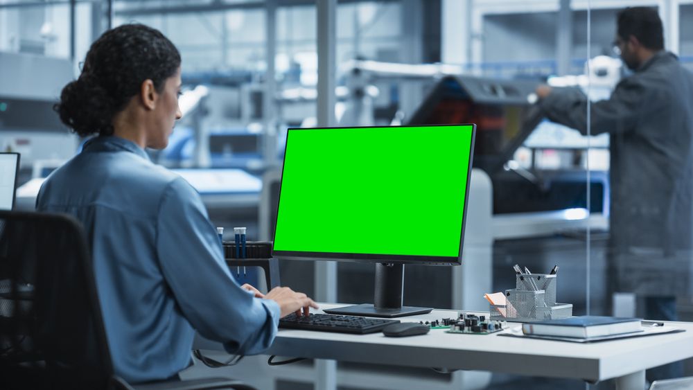 Hispanic Female Robotics Engineer Using Desktop Computer with Green Screen Chromakey Mock Up Display in Factory Office.