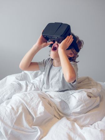 Amazed boy in VR headset in bed