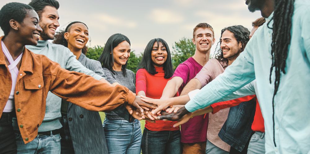 Joyful team of multi-ethnic young people joining hands together outside