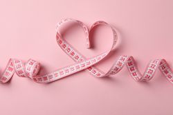 Measuring tape in the form of heart on pink background