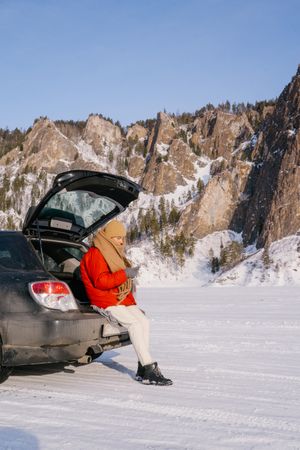 Woman sitting on car trunk in snowy valley