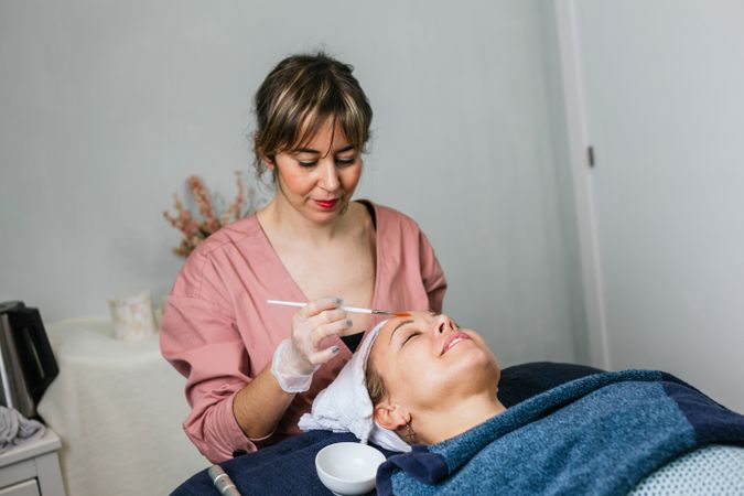 Professional beautician applying facial mask on face of client