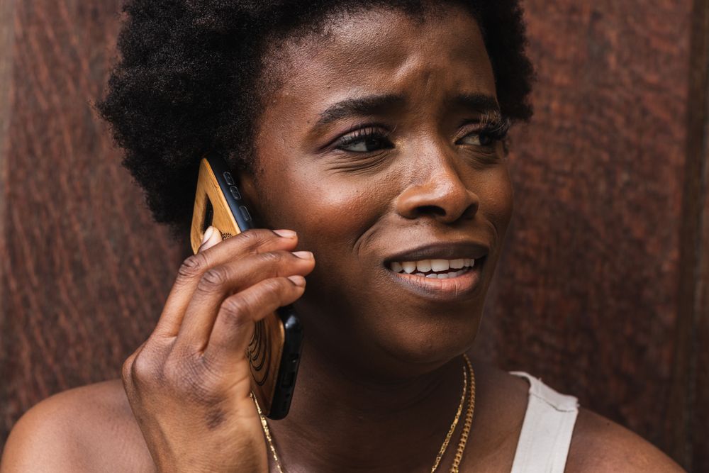 Smiling Black woman talking on smartphone sitting near building