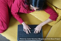 Woman relaxing at home using laptop on yellow sofa 5RvYD5