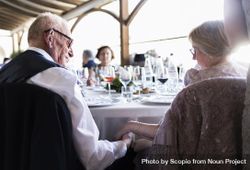 Older couple sitting next to each other at wedding table bxMVj0