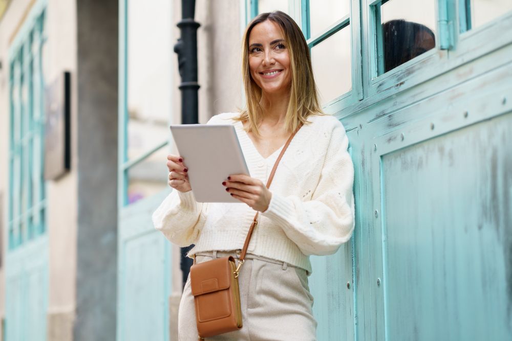 Chic woman in cream standing outside with digital tablet