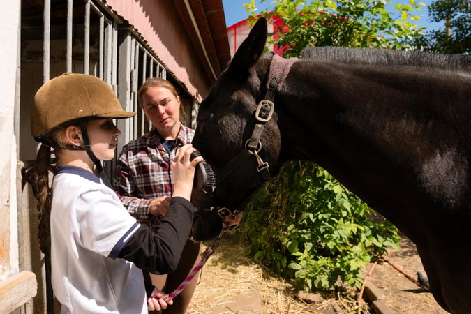 Girl grooming horse with guidance from instructor.