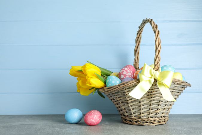 Easter basket filled with colorful eggs and flowers on a wooden background