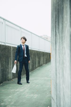 Man in a suit holding a plastic bag standing outdoor