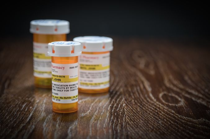 Variety of Non-Proprietary Prescription Medicine Bottles on Reflective Wooden Surface.