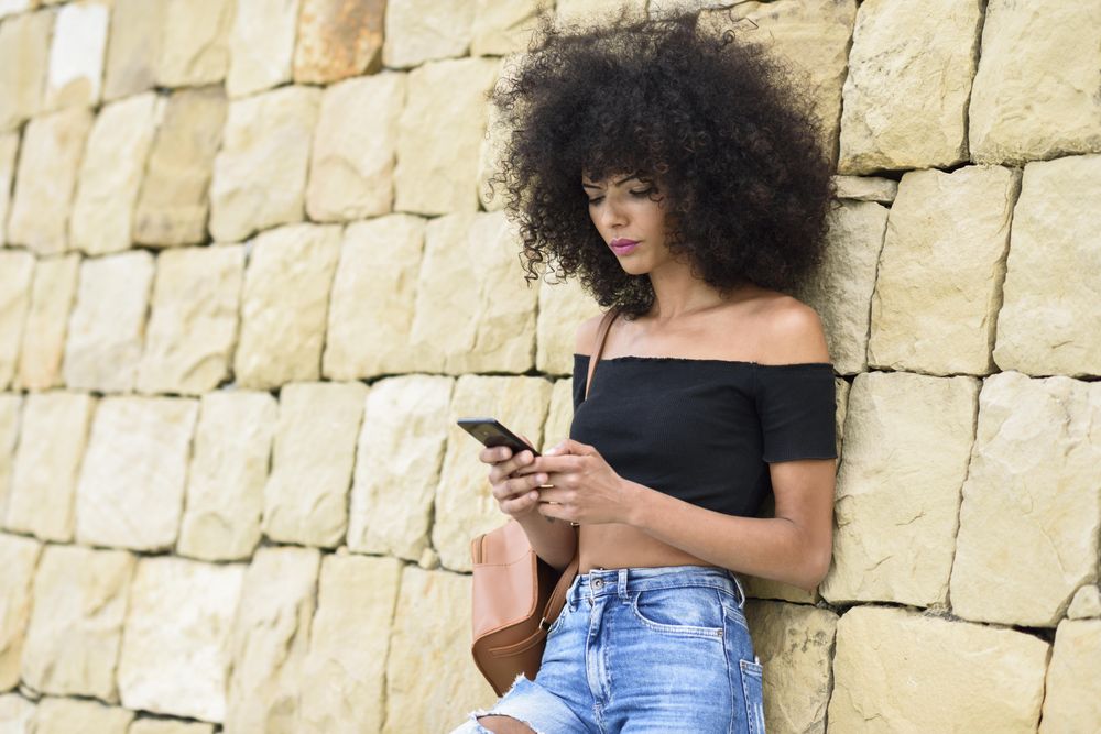 Female texting while leaning on outside wall, copy space