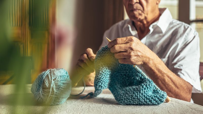 Close up of older man hands knitting with needles and wool yarn