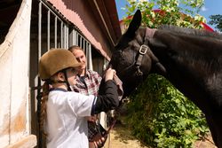 Girl in wipes horse's nose with instructor's guidance.