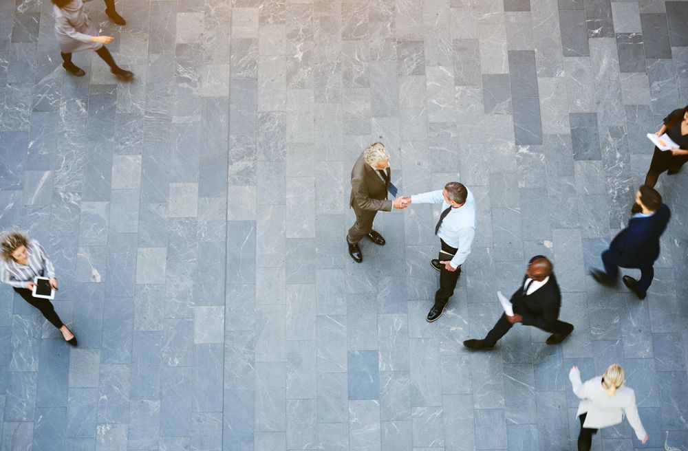 Top view of two businessmen shaking hands in the atrium of a busy office