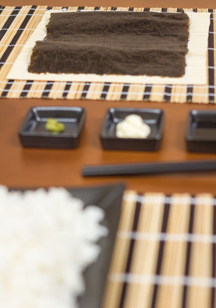 Nori seaweed sheet ready to make Japanese sushi rolls, with sauces and rice in the foreground