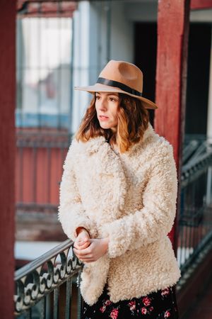 Smiling woman in warm wear standing near building and fence