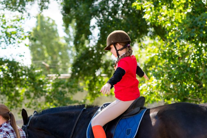 Child rider stretches arms while balancing on horseback.