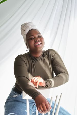 Confident Black female model in turban sitting on white chair