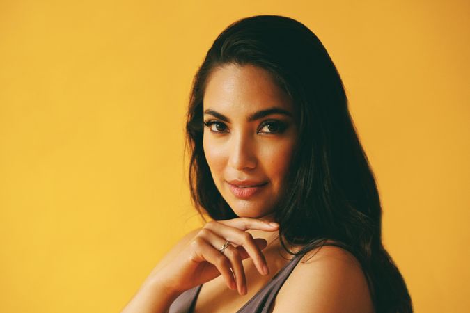 Wistful Hispanic woman looking at camera in yellow room, copy space