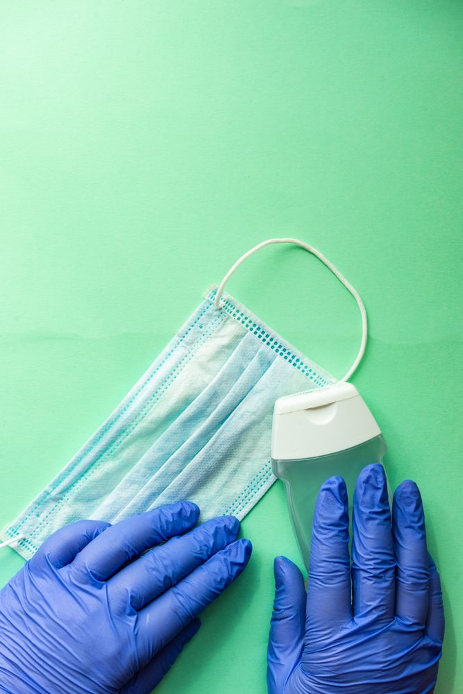 Covid-19 virus concept of hands in latex gloves holding facemask and bottle of anti bacterial wash with copy space
