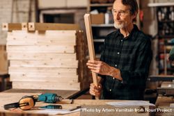 Older man in protective glasses with piece of wood and equipment 42Gqyb