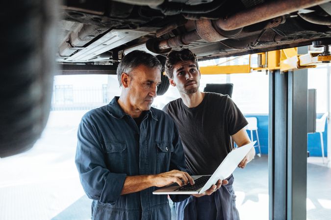Two auto technicians working in auto service station with laptop