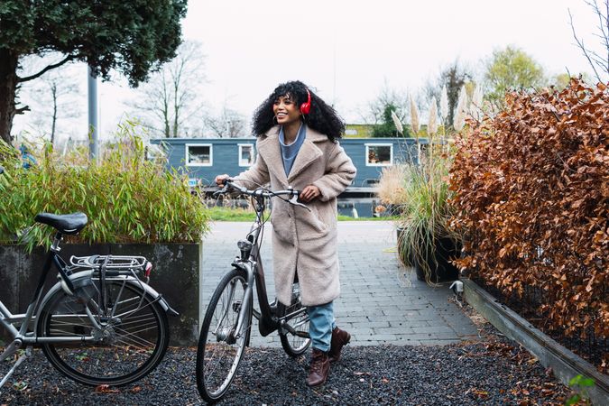Cheerful Black woman in headphones with bicycle