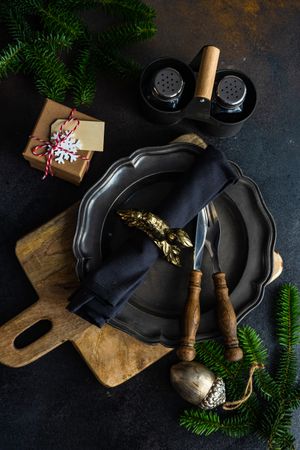 Top view of dark plate with knife and fork on table with pine and gifts