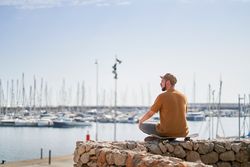 Man in cap relaxed sitting on a skateboard looking out over the harbor