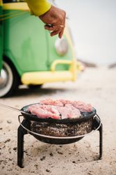 Tanned man cooking on camping stove beside parked mini van