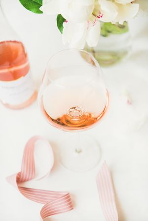 Glass of pink rose wine, and bottle with flowers and ribbon