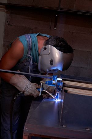 Anonymous man welding metal detail in workshop