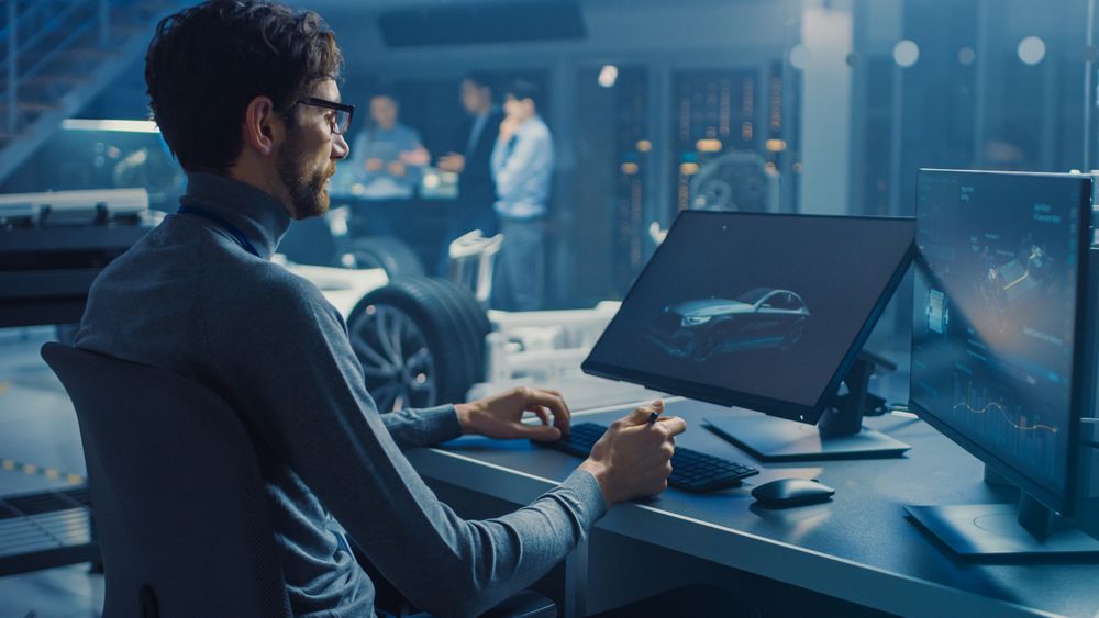 Professional Automotive Graphic Designer is Working on Concept Car Render with a Stylus Pen in a High Tech Innovative Laboratory with a Prototype Car Chassis.