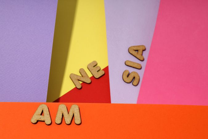 Scattered cork letters spelling “amnesia” on colorful paper background