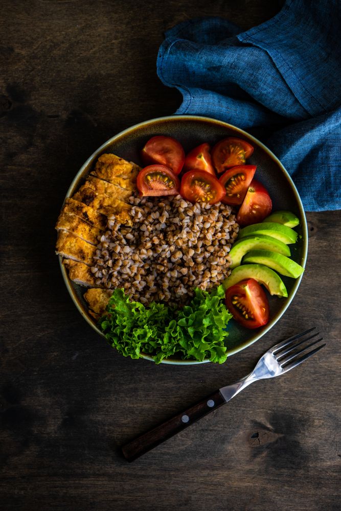 Healthy dinner with buckwheat, lettuce, avocado, and meat on wooden table