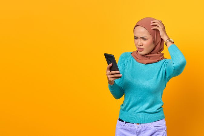 Confused Muslim woman holding her smartphone