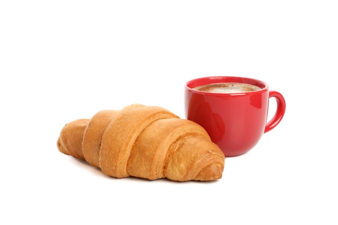 Side view of red cup of coffee and croissant isolated on plain background