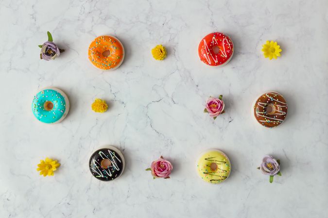 Border of colorful donuts and flowers on marble background