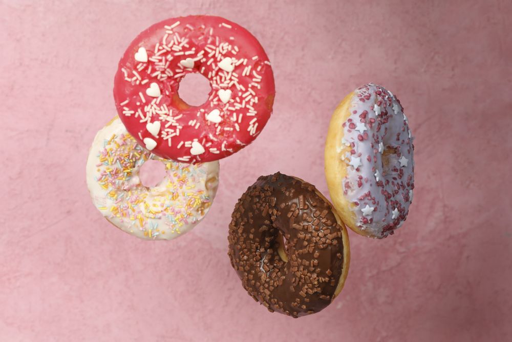 Four different tasty donuts on pink background