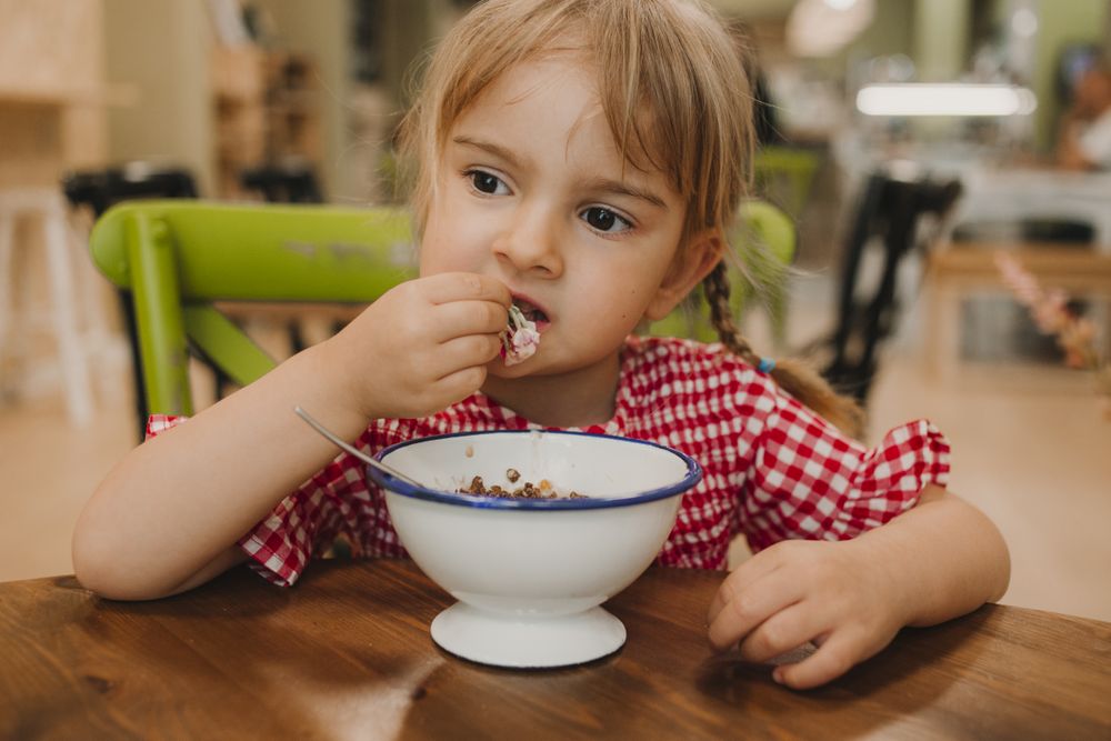 Girl eating with hand from white bowl