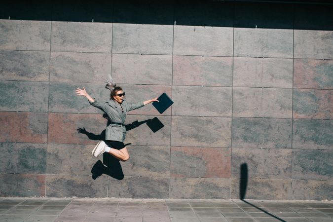 Woman joyfully jumping along wall with tablet