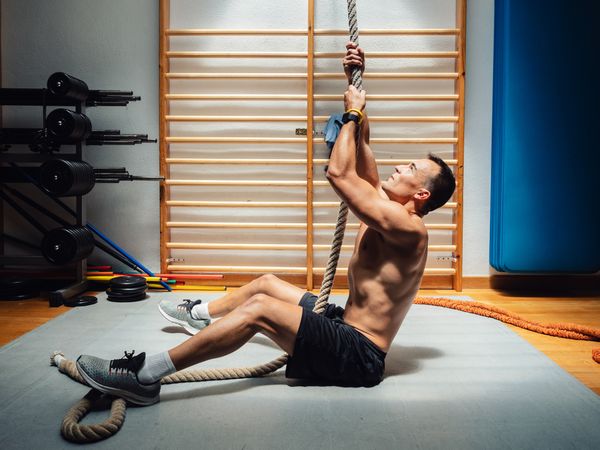 Muscular athlete climbing rope in gym