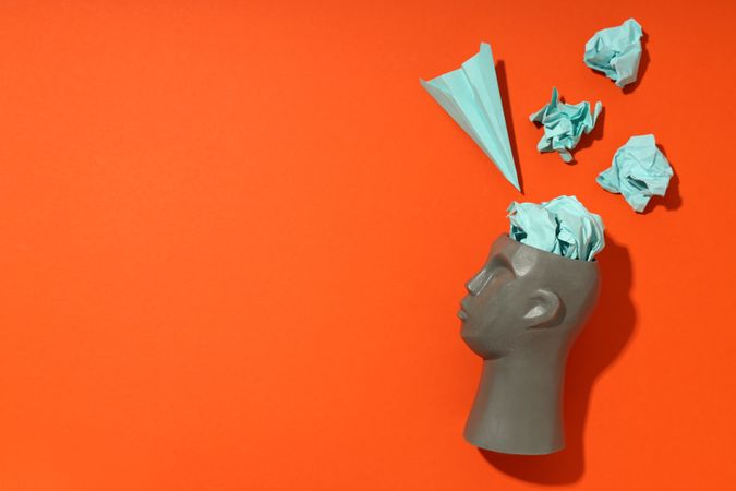 Side of grey bust of head on red background with paper airplane, copy space