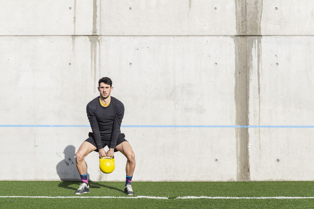 Man training with kettlebell on lawn
